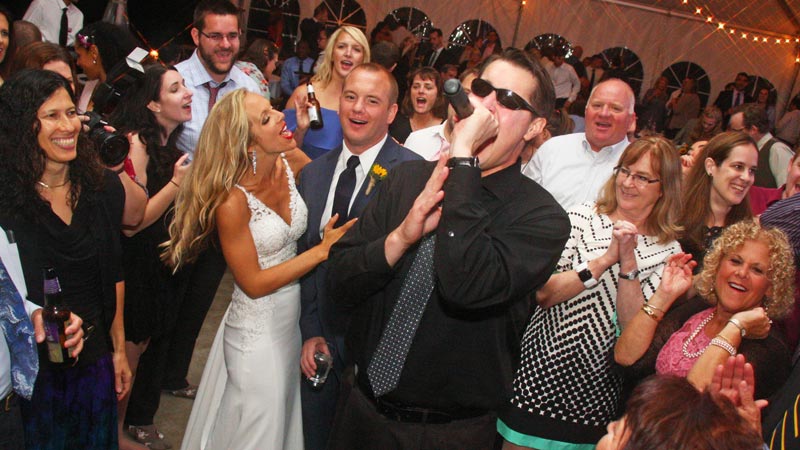 Happy Bride and Groom look on as vocalist Mike perfoms for their guests on a crowded dance floor at this recent Retrospect Band wedding